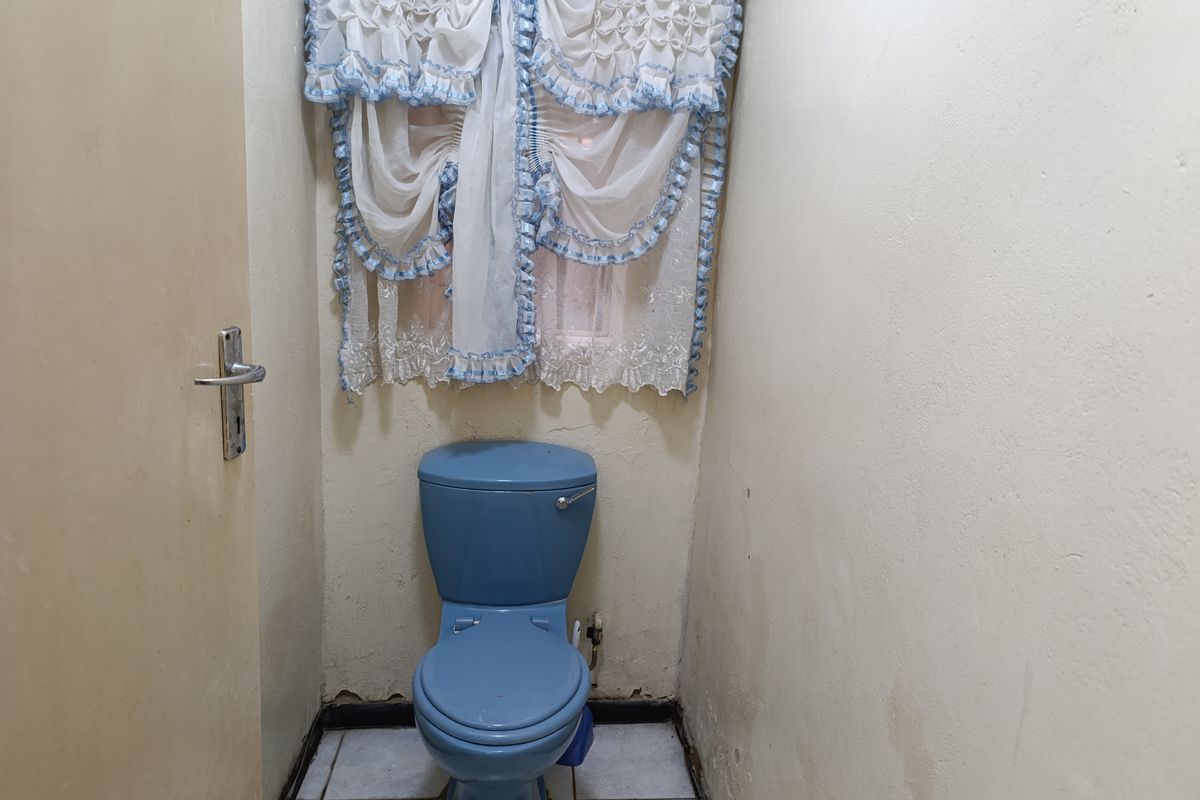 A small powder room featuring a blue toilet, tiled flooring, and dated wall finishes in need of renovation.