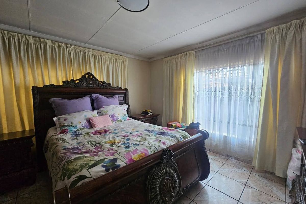 A bedroom featuring tiled flooring and a neutral color palette, offering a functional space with natural light through large windows.
