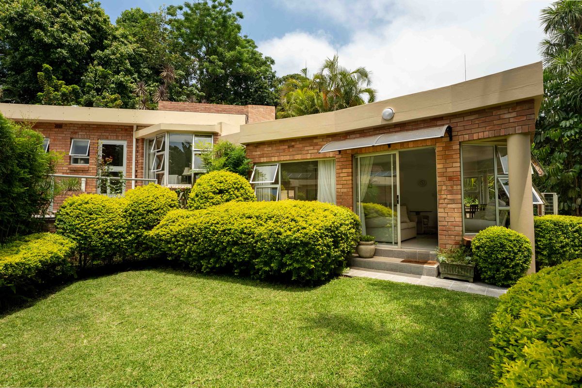 Rear view of the townhouse featuring a brick facade, sliding glass doors leading to a tiled patio, and a well-maintained garden.