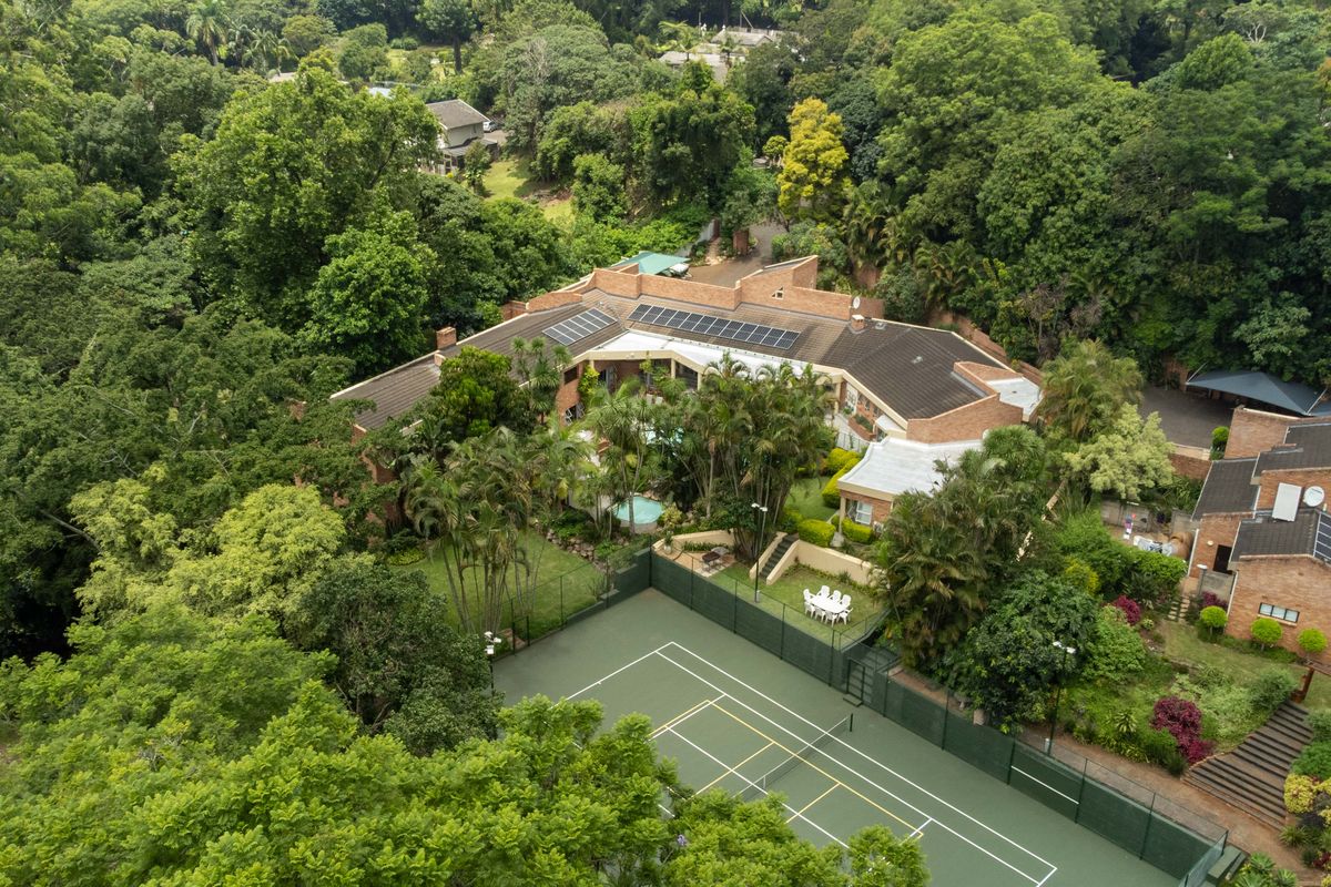 Aerial view of a townhouse complex featuring a private tennis court, swimming pool, lush landscaped gardens, and solar panel installations on the roof.