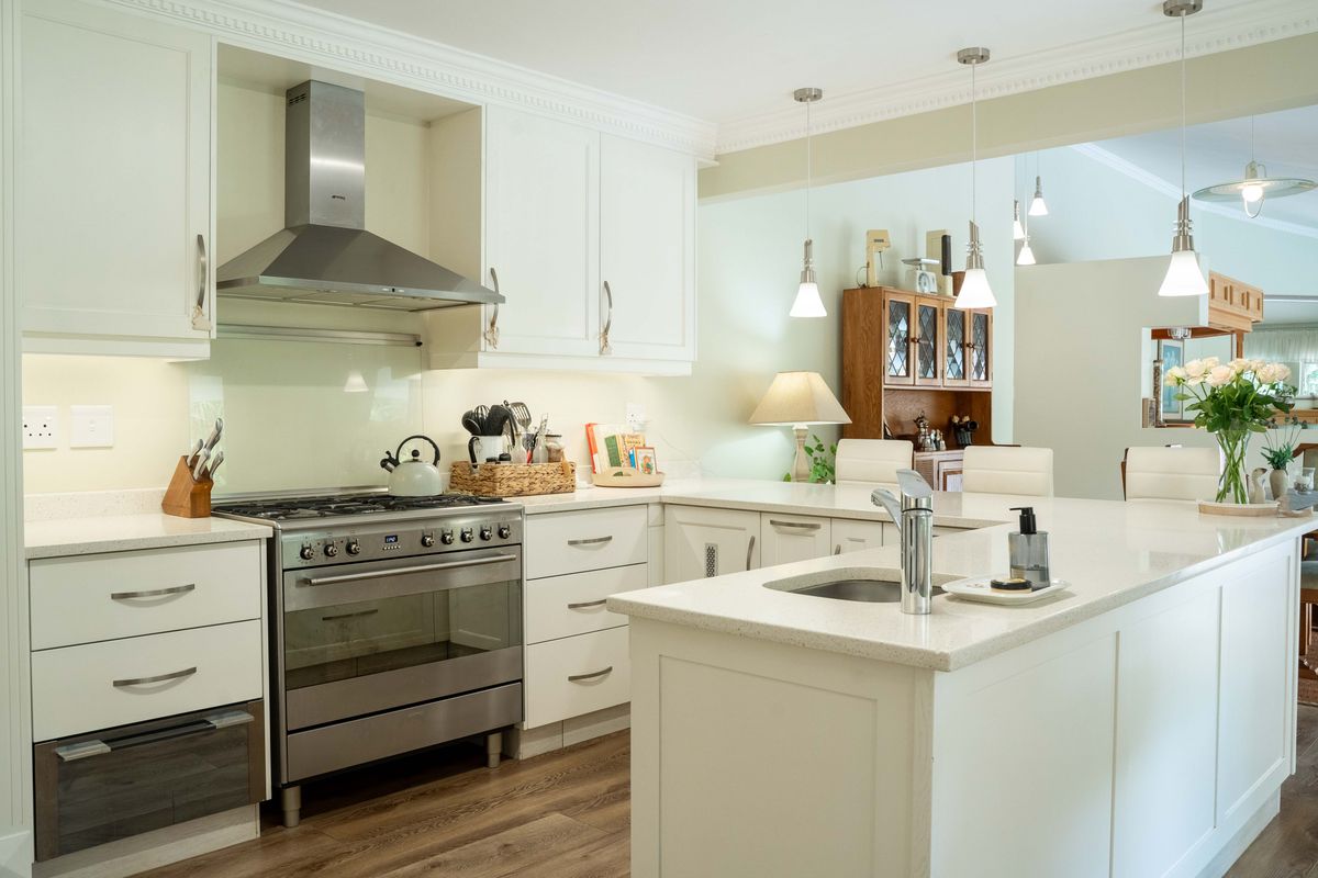 Modern kitchen featuring white shaker cabinetry, quartz countertops, a central island with sink, and high-end stainless steel appliances including a gas range and extractor.