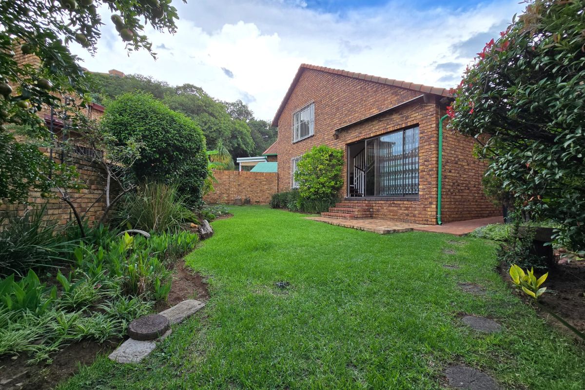 A view of the rear garden featuring a well-maintained lawn, established landscaping, and a brick-faced exterior with sliding glass doors.