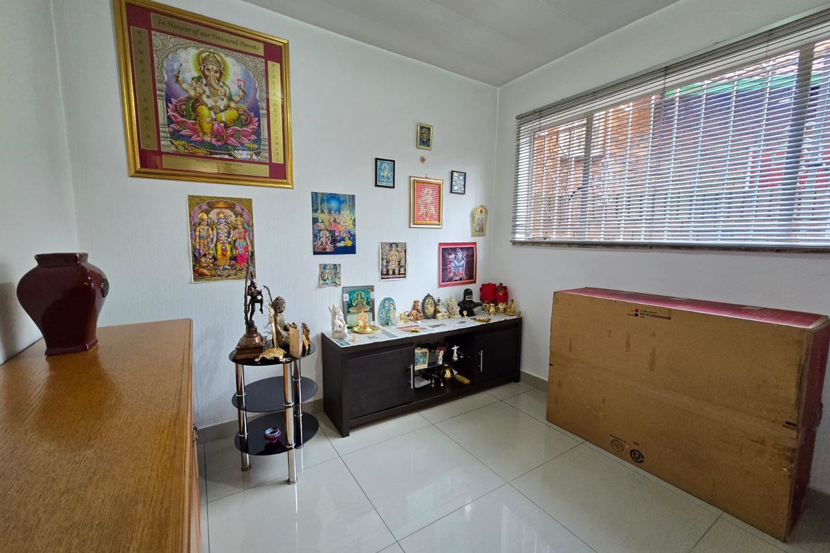 A bright room featuring neutral tiled flooring and horizontal window blinds, currently utilized as a prayer or display space.