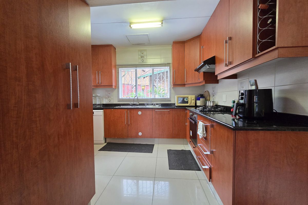 A functional kitchen featuring cherry wood cabinetry, black granite countertops, a built-in oven, gas hob, and tiled flooring.