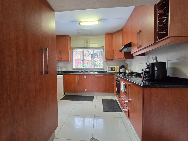 A functional kitchen featuring cherry wood cabinetry, black granite countertops, a built-in oven, gas hob, and tiled flooring.