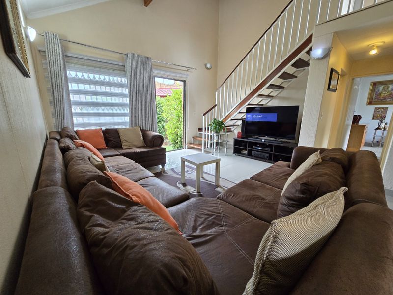 Spacious open-plan living area featuring high vaulted ceilings, tiled flooring, and a staircase leading to an upper level with direct access to the garden.