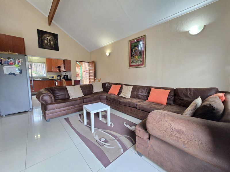 Open plan living area featuring vaulted ceilings with exposed timber beams, tiled flooring, and direct access to the kitchen and outdoor area.