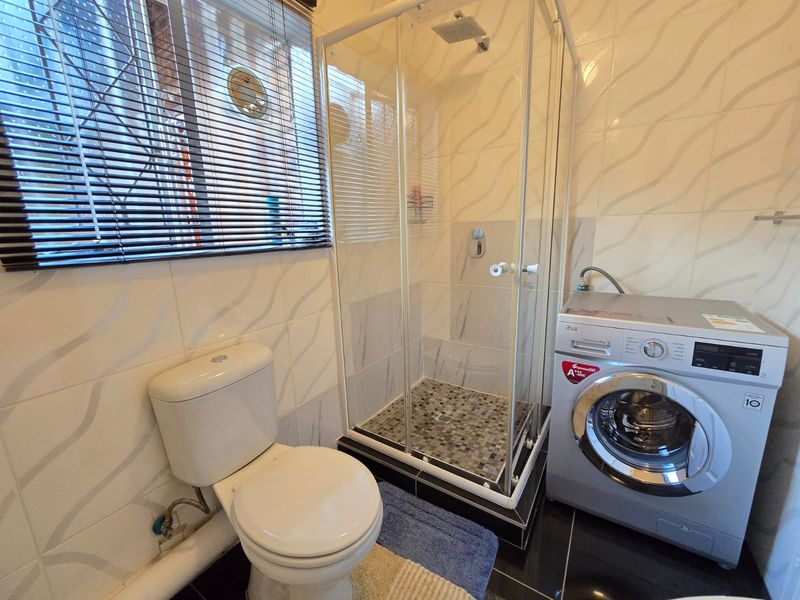A functional bathroom featuring a glass-enclosed shower, a standard toilet, and a dedicated space for a washing machine with tiled walls and flooring.