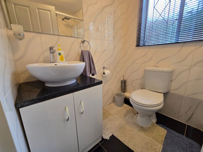 A compact bathroom featuring a modern vessel sink on a vanity cabinet, a toilet, and tiled walls with a window.