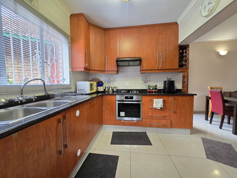 A functional kitchen featuring wood-finish cabinetry, granite countertops, a built-in oven, and a gas hob with an extractor fan.