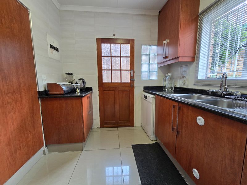 A functional kitchen featuring wood-veneer cabinetry, dark granite countertops, a double stainless steel sink, and a rear exterior door with glass paneling.