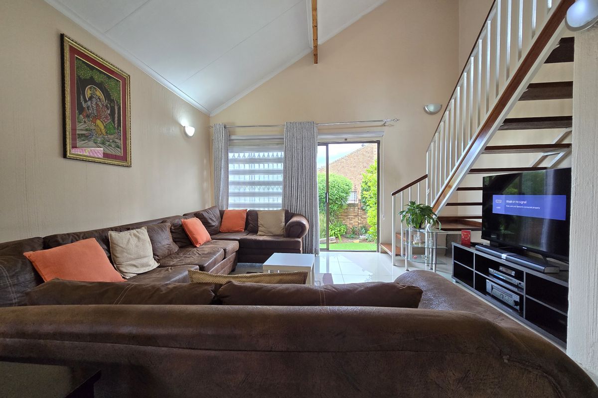 Spacious living room with high vaulted ceilings, tiled flooring, and a staircase leading to the upper level, featuring sliding doors to the garden.