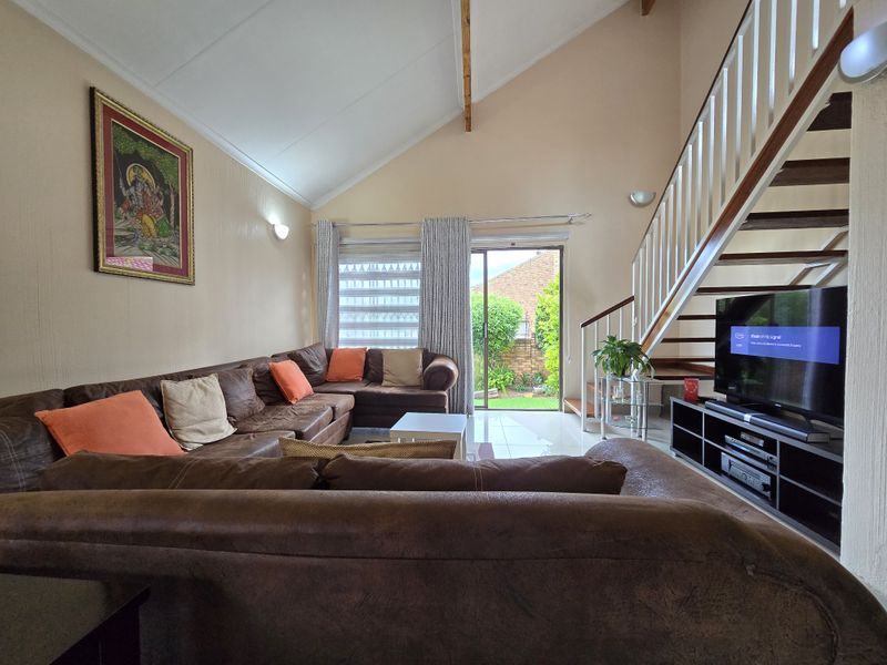 Spacious living room with high vaulted ceilings, tiled flooring, and a staircase leading to the upper level, featuring sliding doors to the garden.