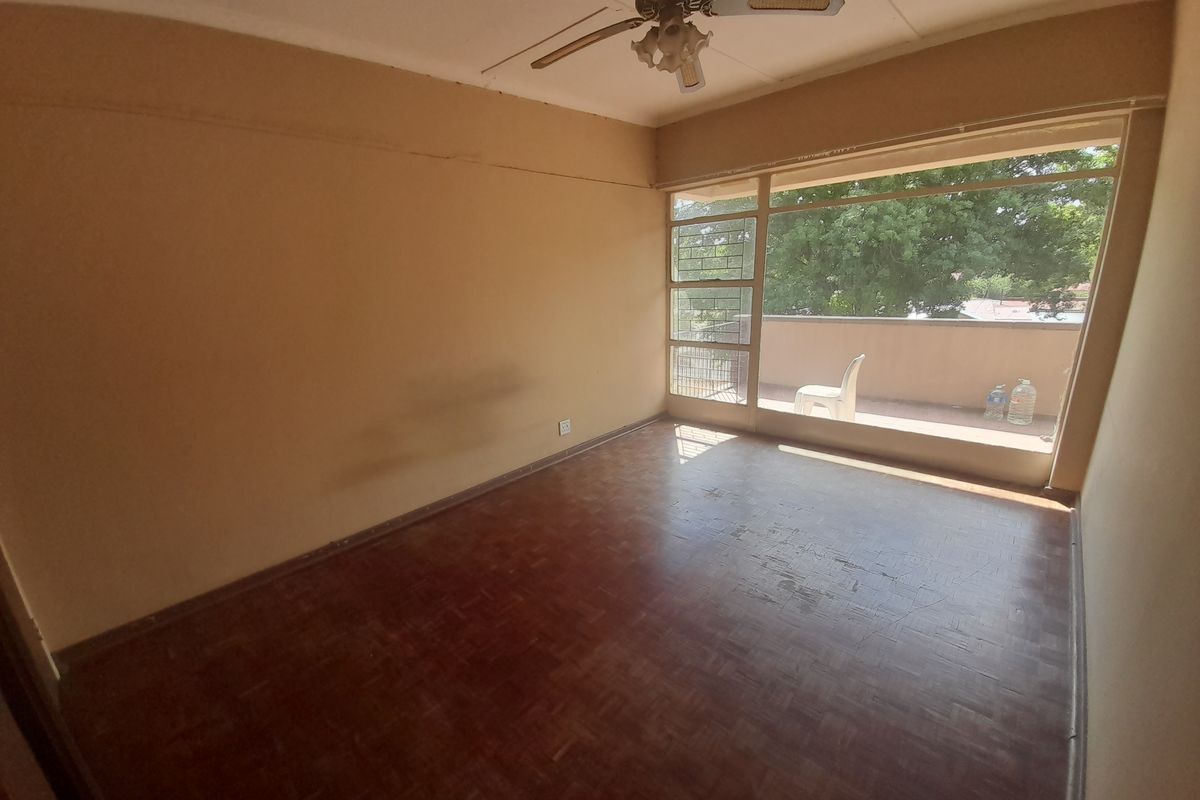 A spacious, empty bedroom featuring original parquet flooring, a ceiling fan, and large windows providing access to an outdoor balcony area.