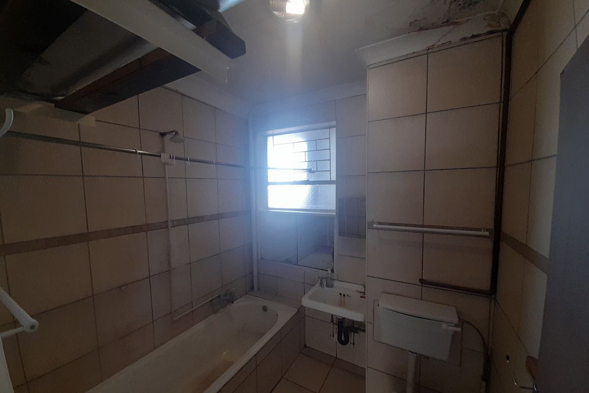 A dated bathroom featuring a bathtub, wall-mounted basin, and toilet, requiring significant renovation and repair to the ceiling and wall finishes.
