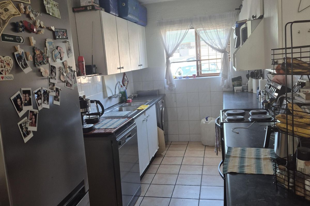 A functional galley-style kitchen featuring tiled flooring, laminate countertops, built-in cabinetry, and a window providing natural light.