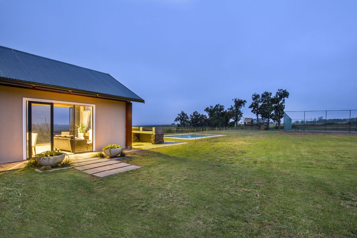 A view of the rear exterior featuring a spacious lawn, a swimming pool, and a covered patio area adjacent to the main dwelling.