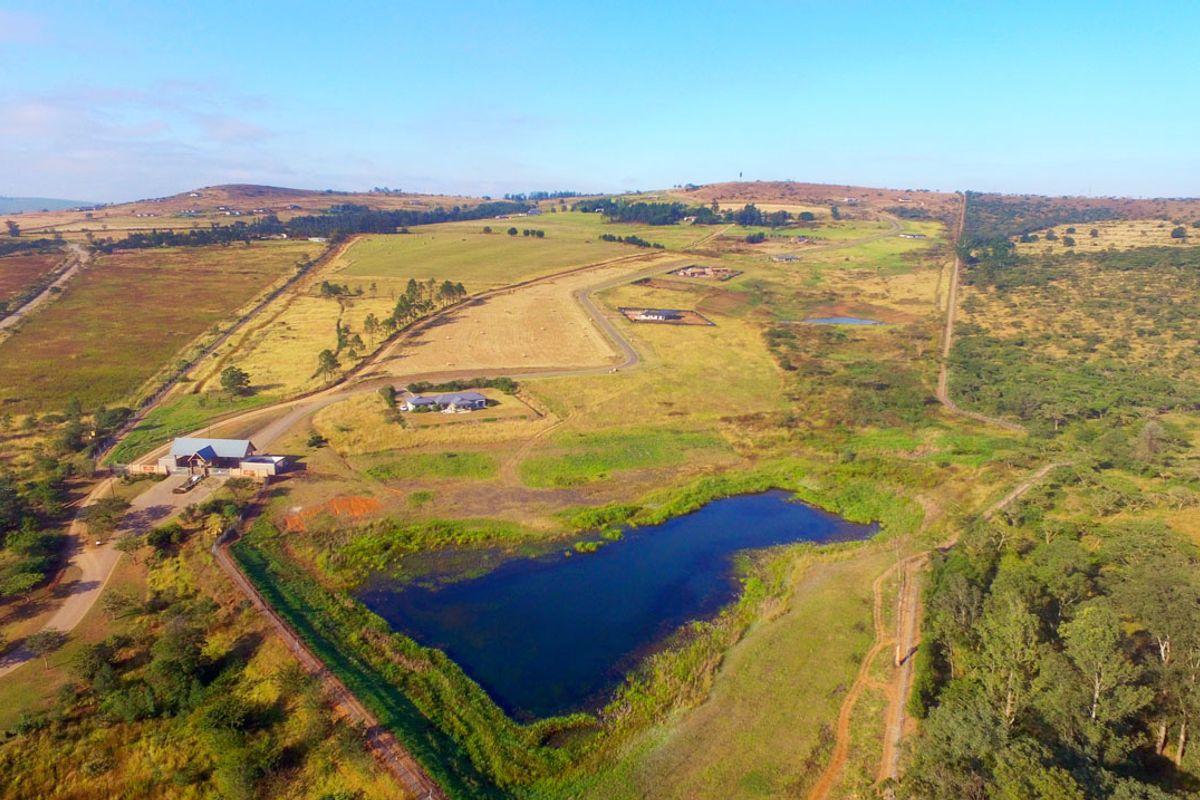 Aerial view of a large residential land parcel featuring rolling hills, natural vegetation, and a scenic dam.