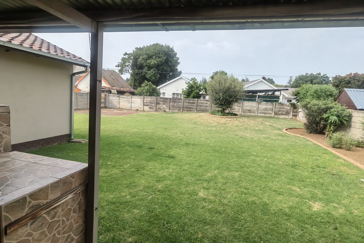 Spacious rear garden featuring a lawn, precast boundary wall, and a covered patio area with a built-in tiled braai.