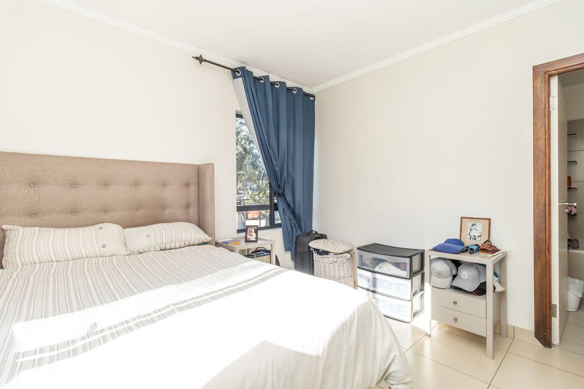 A bright bedroom featuring tiled flooring, a window with curtain rod, and a doorway leading to an adjacent bathroom.
