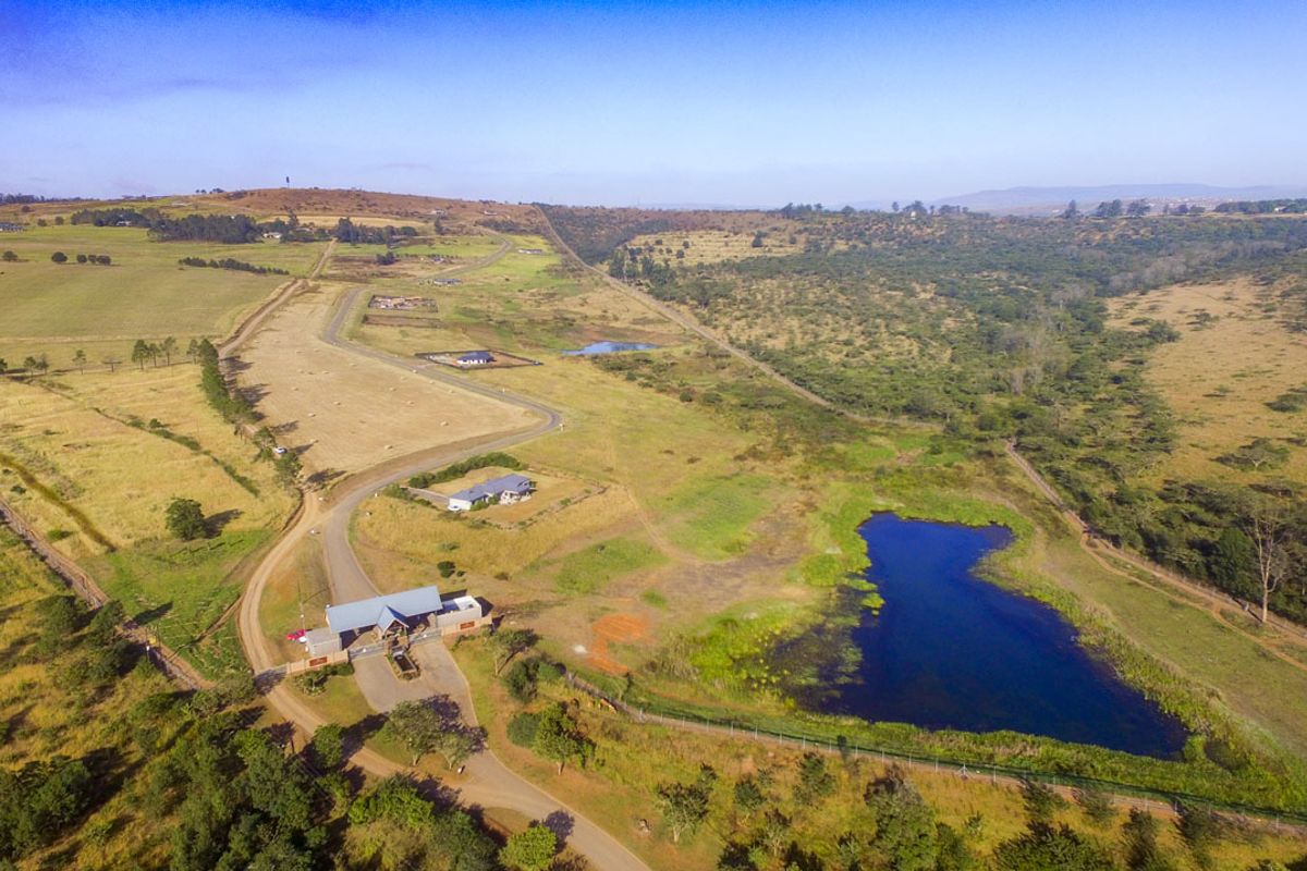 Aerial view of a residential estate featuring open land, a natural pond, and a gated entrance structure.