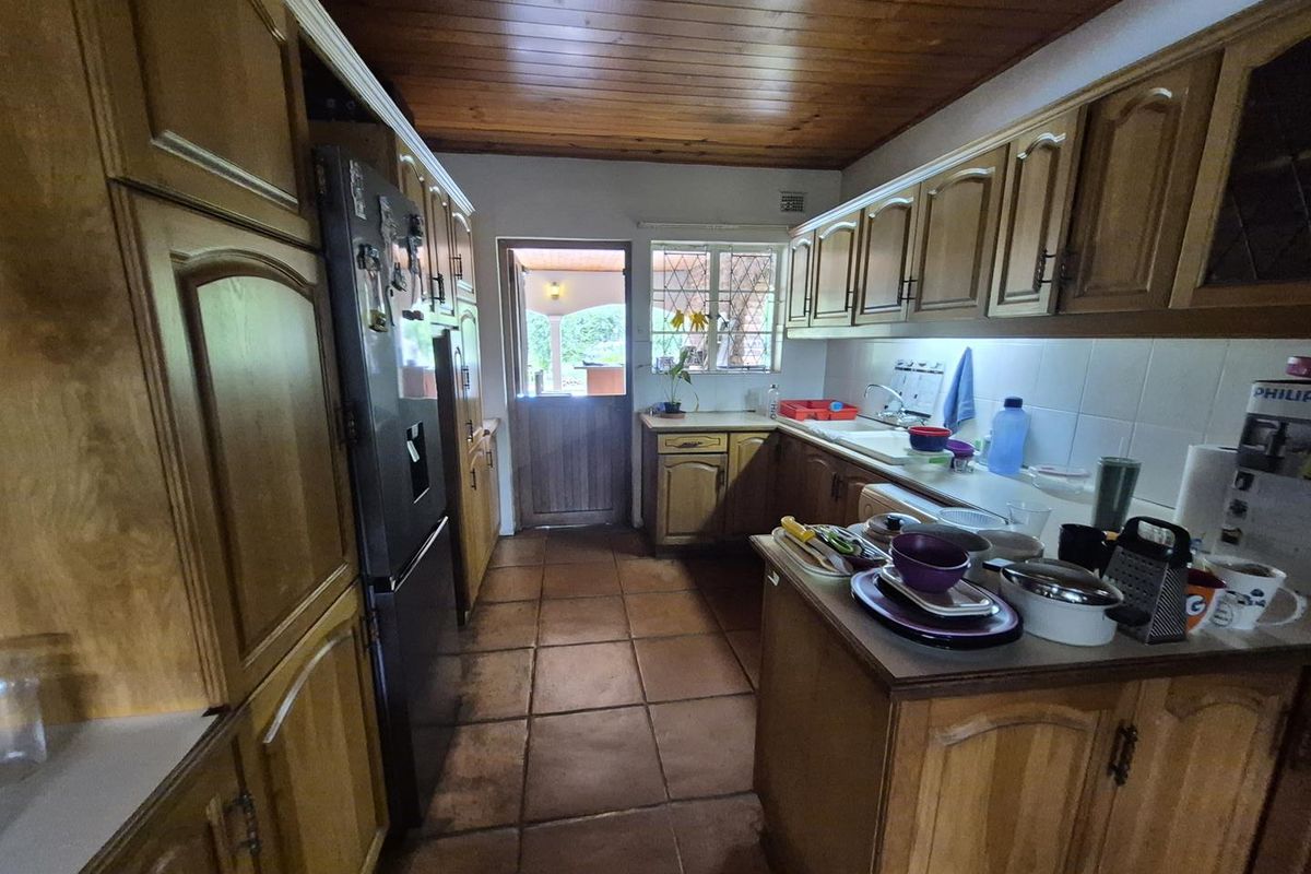 A functional kitchen featuring wooden cabinetry, tiled flooring, and a timber-paneled ceiling, with direct access to an outdoor area.