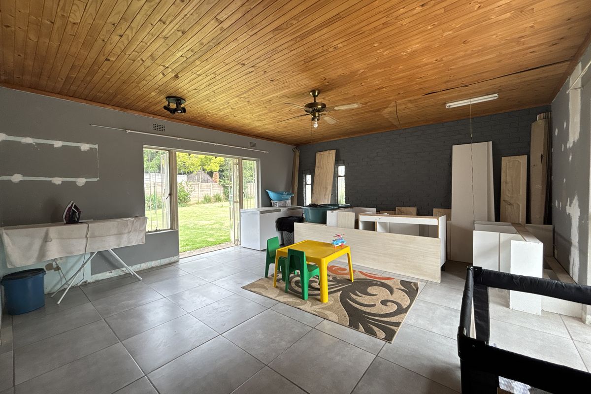 Spacious living area featuring a timber ceiling, tiled floors, and sliding doors leading to the garden, currently undergoing renovation with unfinished wall surfaces.