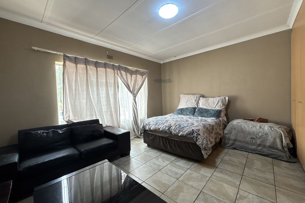 A spacious bedroom featuring tiled flooring, a built-in cupboard, and a large window with security bars, offering a functional living space.