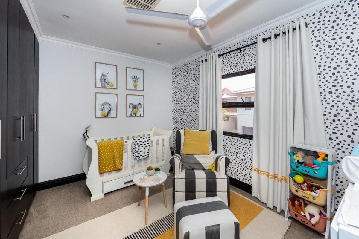 A well-maintained bedroom featuring built-in cupboards, ceiling fan, and decorative wallpaper, providing a functional and comfortable space.