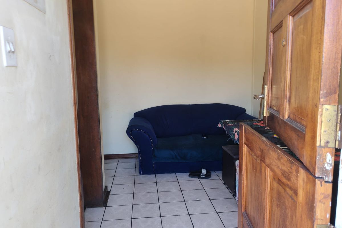 A small living area featuring tiled flooring and a wooden door frame, currently in need of cosmetic updates to improve its overall appeal.