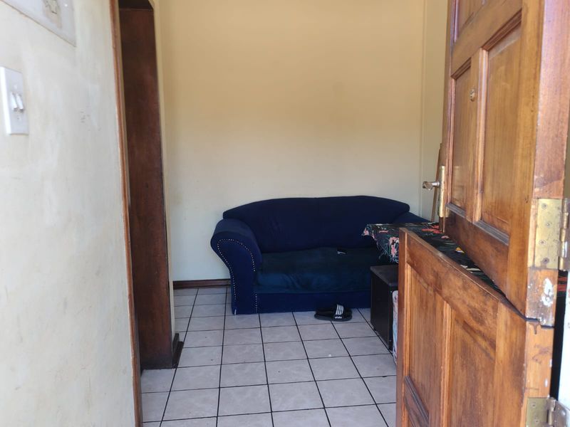 A small living area featuring tiled flooring and a wooden door frame, currently in need of cosmetic updates to improve its overall appeal.