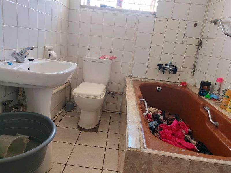 A dated bathroom featuring a pedestal basin, toilet, and built-in bathtub with tiled finishes, requiring renovation to update the fixtures and wall tiling.