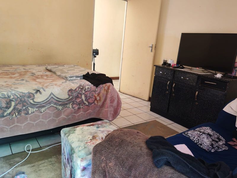 A bedroom featuring tiled flooring and access to an adjoining room, currently showing signs of wear on the wall surfaces.