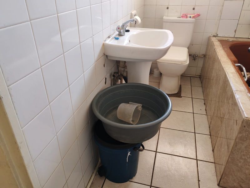 A dated bathroom featuring a pedestal basin, toilet, and tiled bathtub, requiring significant renovation and modernization of finishes and fixtures.