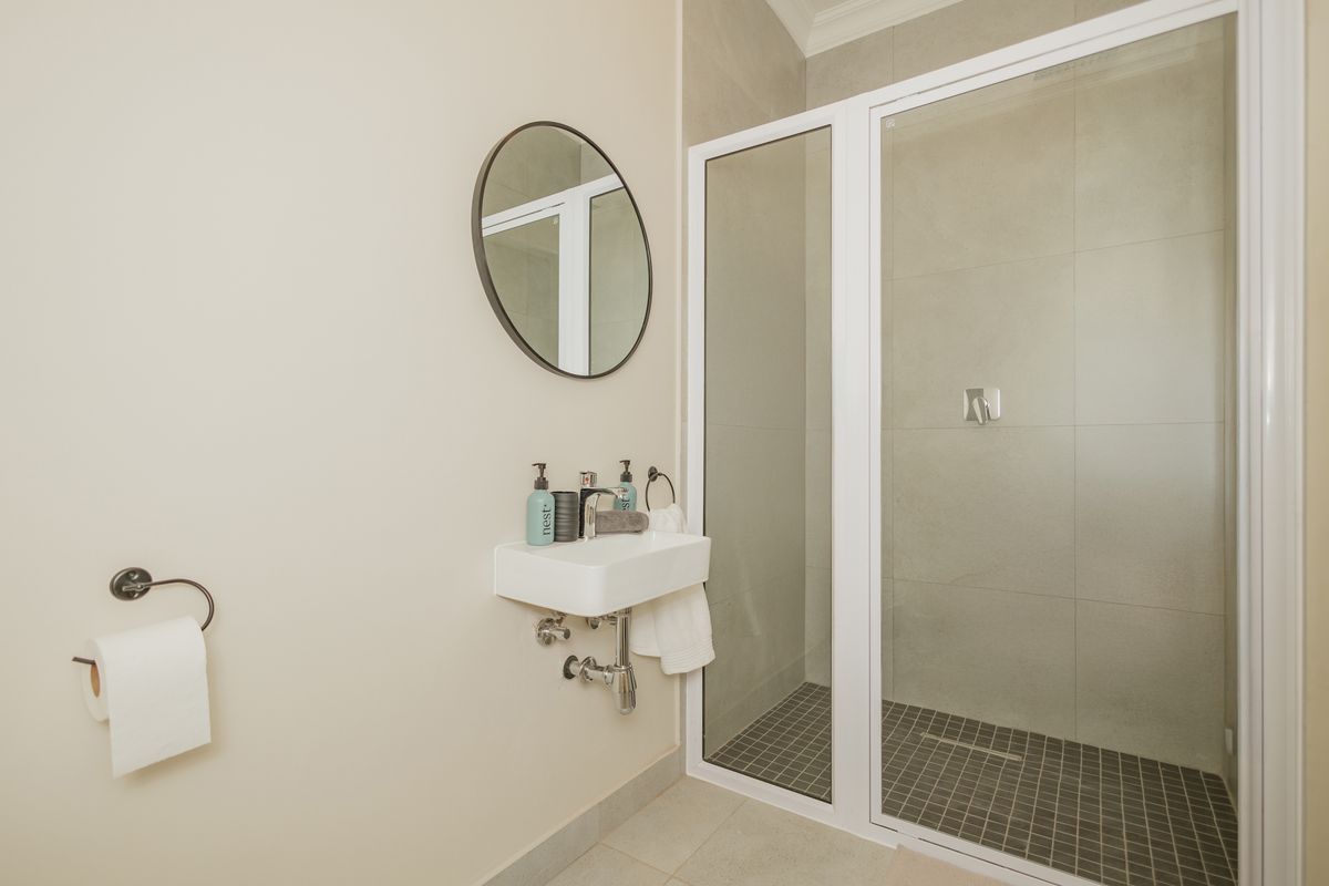A modern bathroom featuring a wall-mounted basin, chrome fixtures, and a walk-in shower with a tiled floor and white frame.