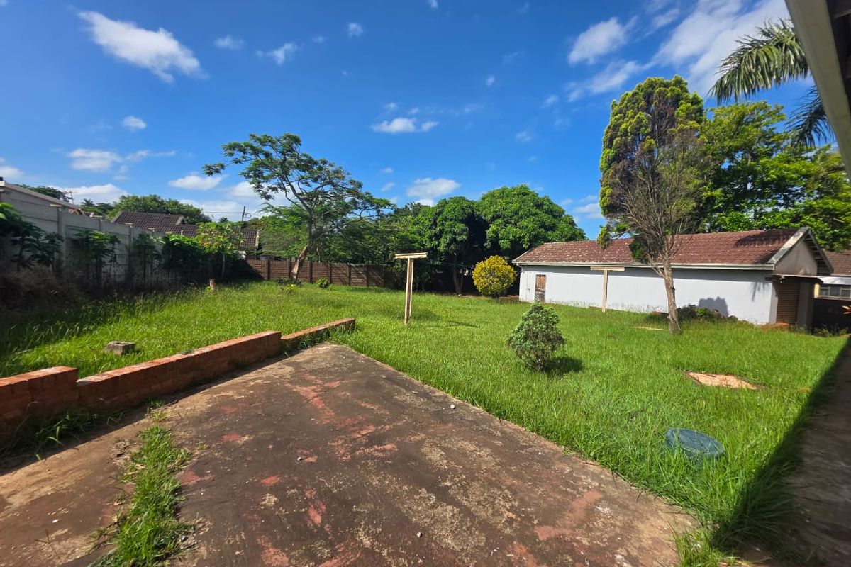 A spacious rear garden featuring a concrete patio area, a brick retaining wall, and an outbuilding, set within a fenced perimeter.