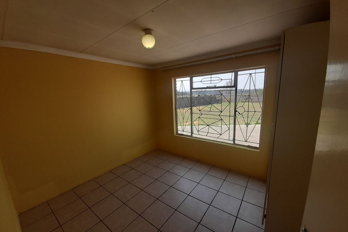 A vacant bedroom featuring tiled flooring, yellow painted walls, and a large window with security bars overlooking the rear yard.