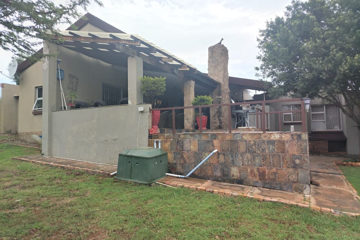 A rear exterior view of the house featuring a covered patio area with stone cladding, a built-in chimney, and a surrounding garden.