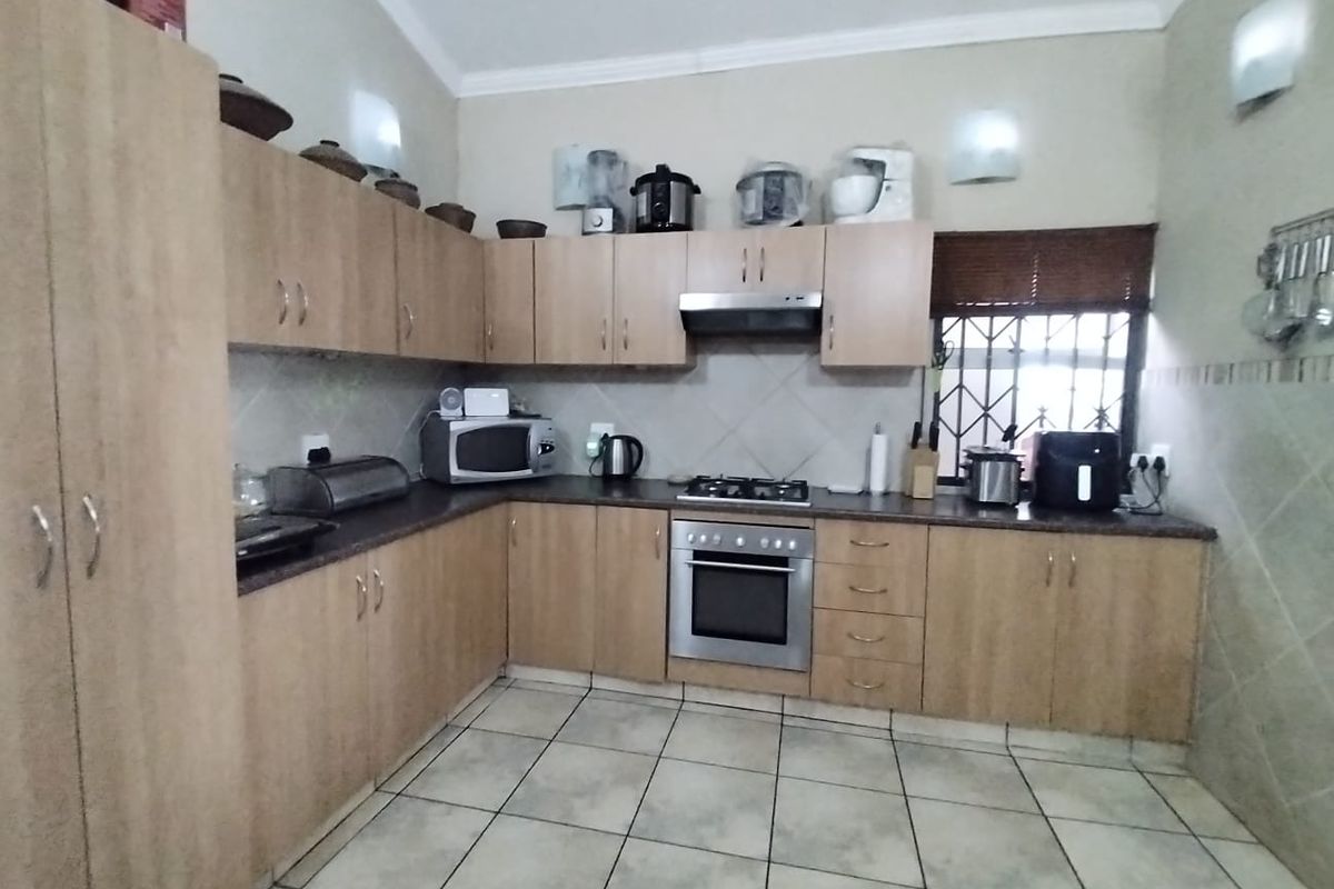 A functional kitchen featuring light wood cabinetry, tiled flooring, a built-in oven, gas hob, and extractor fan with a window security gate.