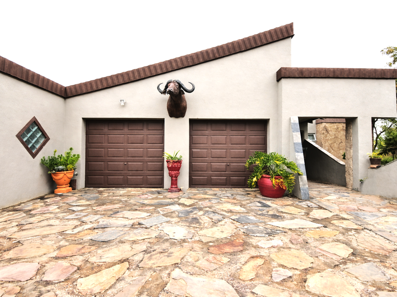 Front elevation of the property featuring a double garage with brown sectional doors, stone-paved driveway, and unique architectural detailing.