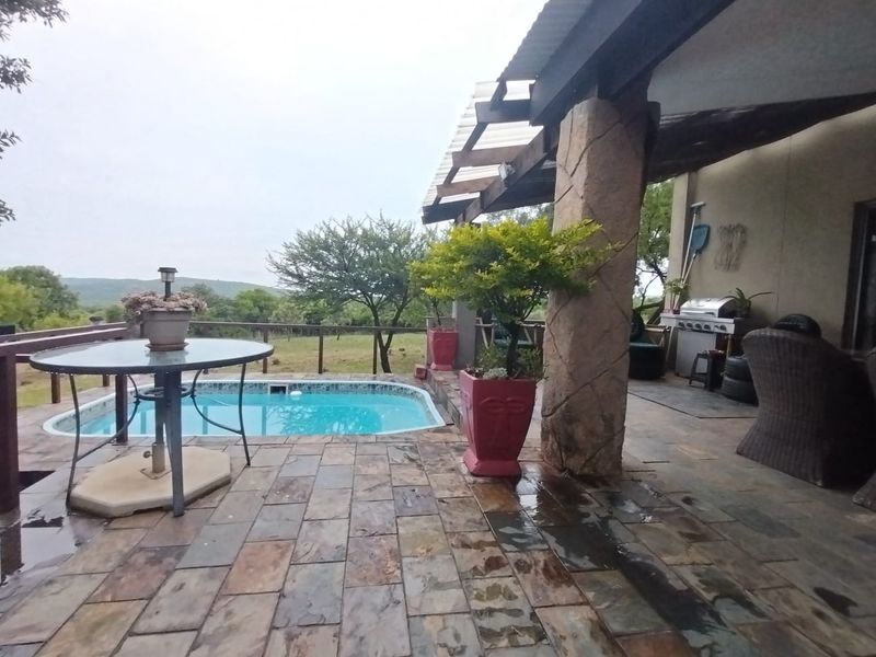 Covered outdoor patio area featuring stone flooring, a structural stone pillar, and direct access to a swimming pool with scenic landscape views.