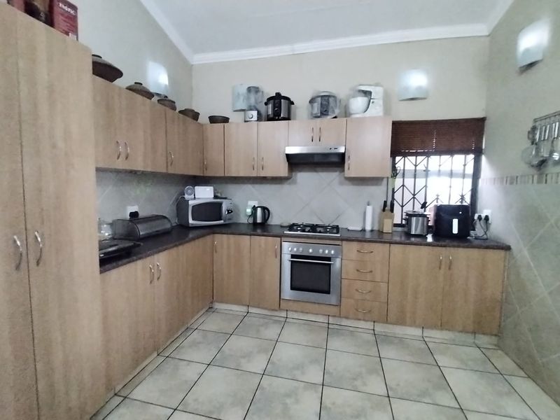 A functional kitchen featuring light wood cabinetry, tiled flooring, a built-in oven, gas hob, and extractor fan with a window security gate.