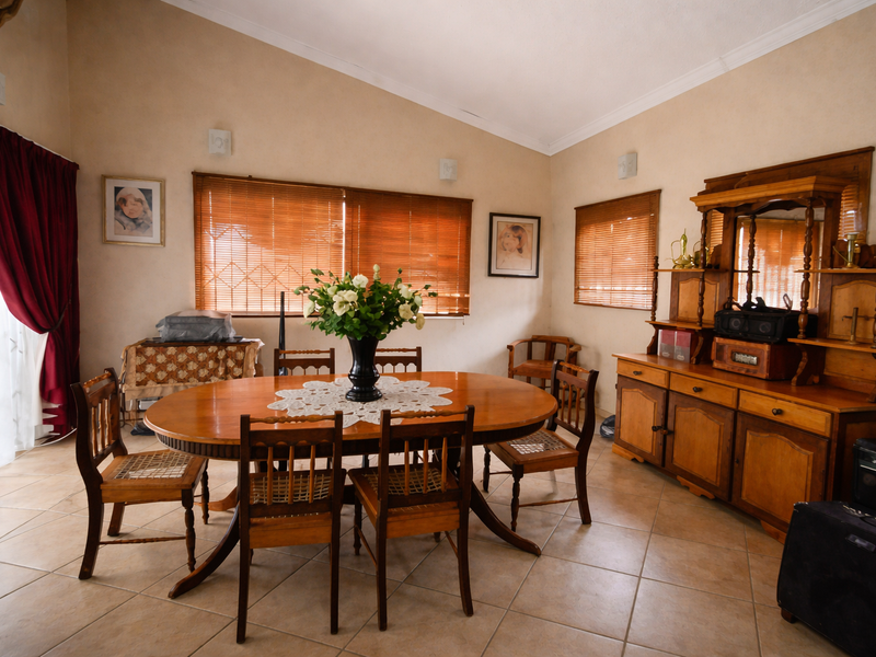 A dining room featuring vaulted ceilings, tiled flooring, and large windows with wooden blinds, providing a bright and functional space for family meals.