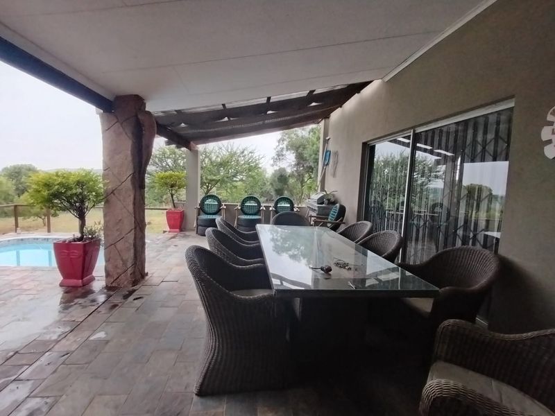 Covered outdoor patio area featuring tiled flooring, a decorative stone-clad support pillar, and direct access to the swimming pool and garden.