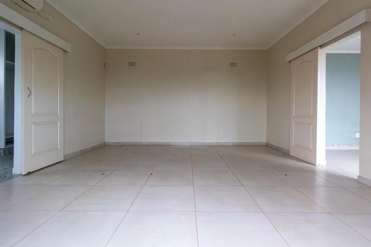 An empty, neutrally painted living room featuring tiled flooring, recessed lighting, and dual sliding door access to adjacent spaces.