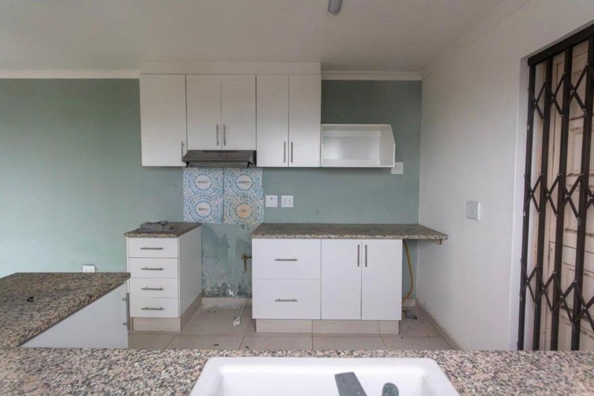 A functional kitchen space featuring granite countertops, white cabinetry, and an extractor fan, currently requiring minor repairs to the wall and backsplash area.