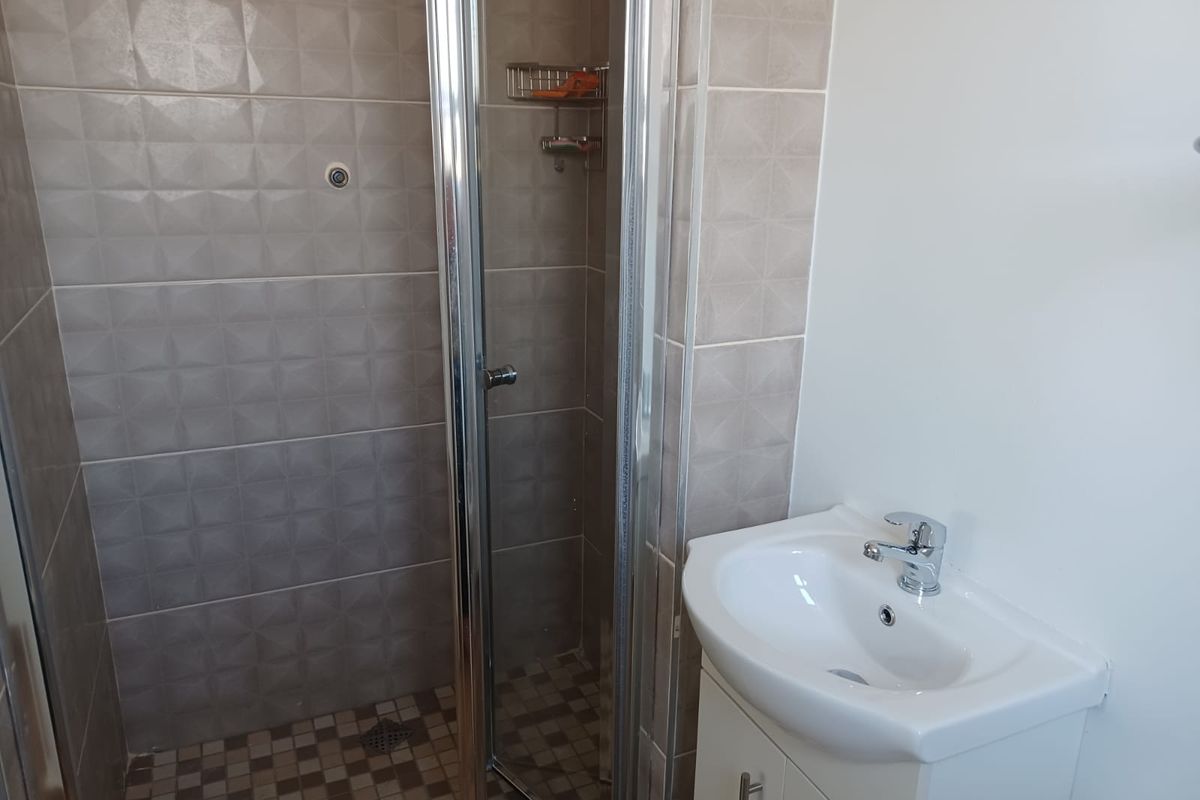 A clean, functional bathroom featuring a glass-enclosed shower with textured wall tiles and a modern vanity basin with chrome fixtures.