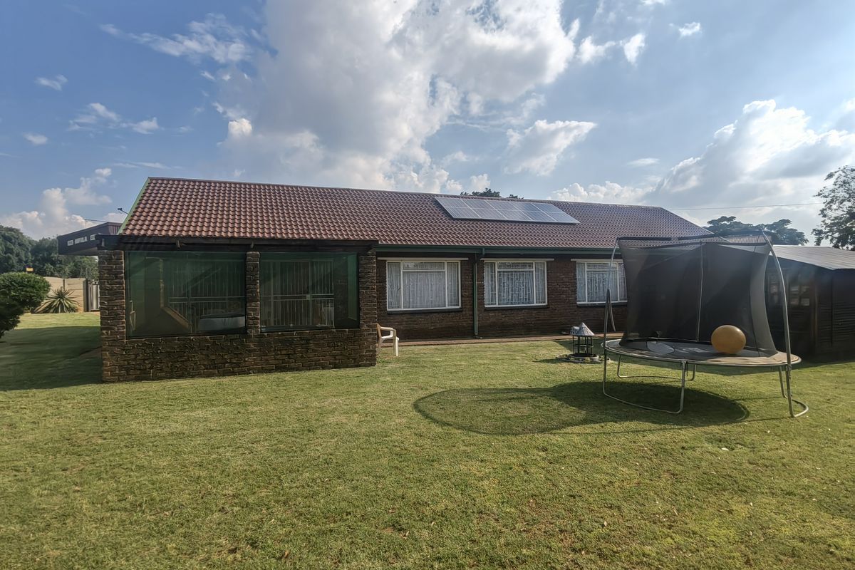 Rear view of a brick house featuring a tiled roof with solar panels, an enclosed patio area, and a spacious lawn.