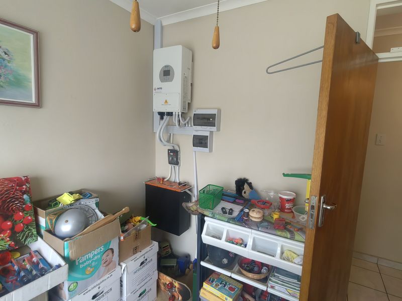 Utility area featuring a wall-mounted solar inverter, battery storage system, and electrical distribution board with exposed conduit wiring.