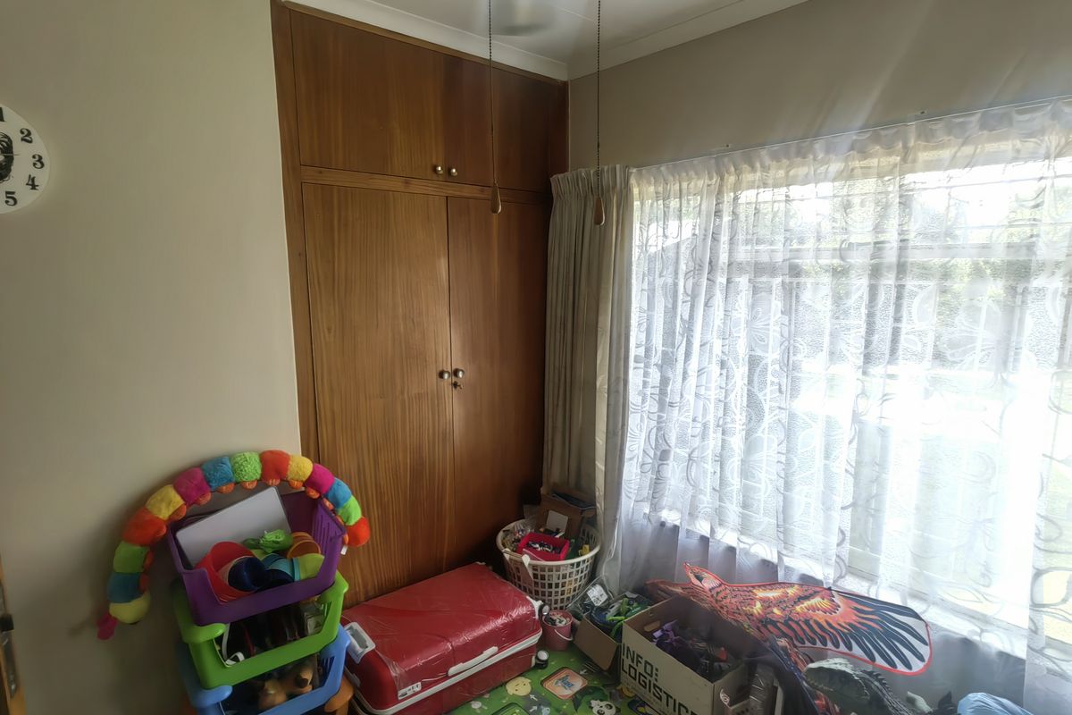 A bedroom featuring a built-in wooden wardrobe and a ceiling fan, with natural light entering through the window.